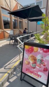 パラソル付きの丸テーブルが並ぶスターバックス横浜荏田西店のテラス席。入口にはストロベリーの季節メニュー看板