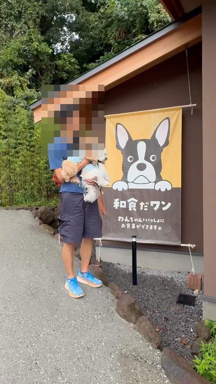和食だワンの壁画の前で2匹の犬を抱いて立つ